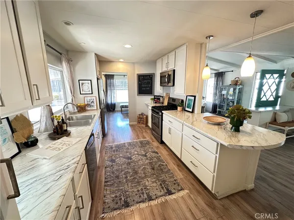a large white open kitchen with stainless steel appliances kitchen island granite countertop a stove a sink dishwasher and white cabinets with wooden floor