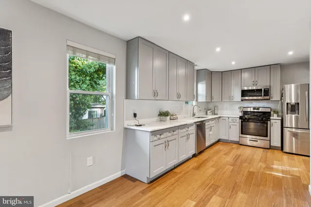 a kitchen with stainless steel appliances granite countertop a stove top oven a sink dishwasher and a refrigerator with wooden floor