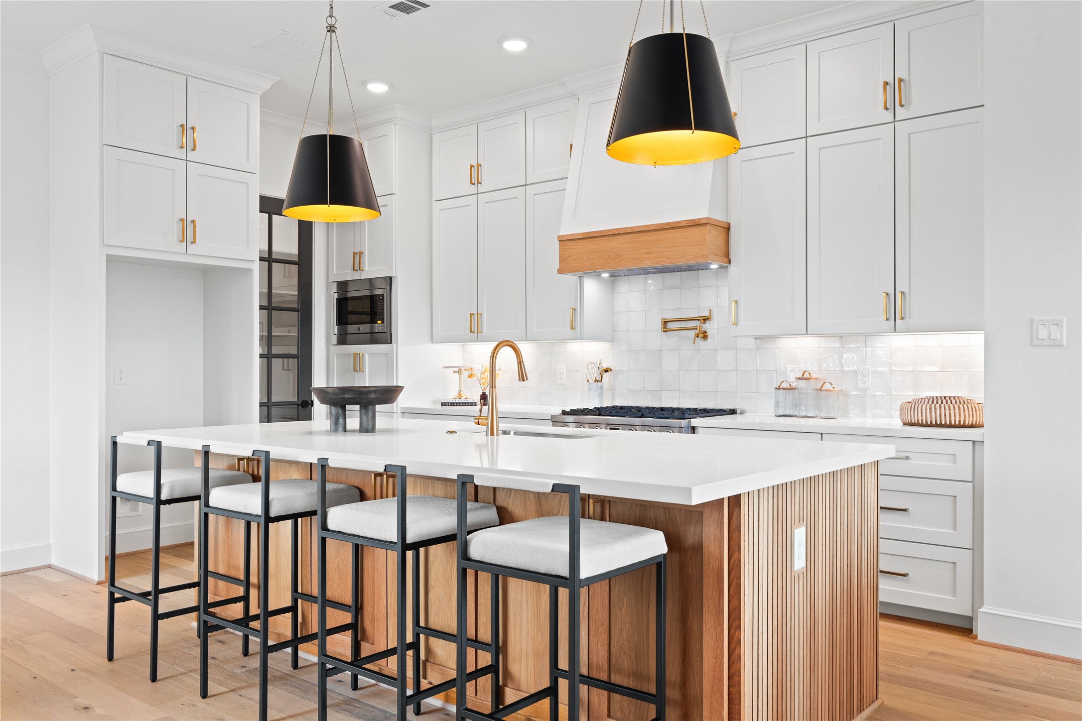 1614 Ojeman Road, Unit J Houston, TX 77055 - Photo 14 of 50 Modern kitchen featuring a spacious quartz island, custom cabinetry, and striking black pendant lights that create a bold contrast against the warm wood accents and white oak floors.