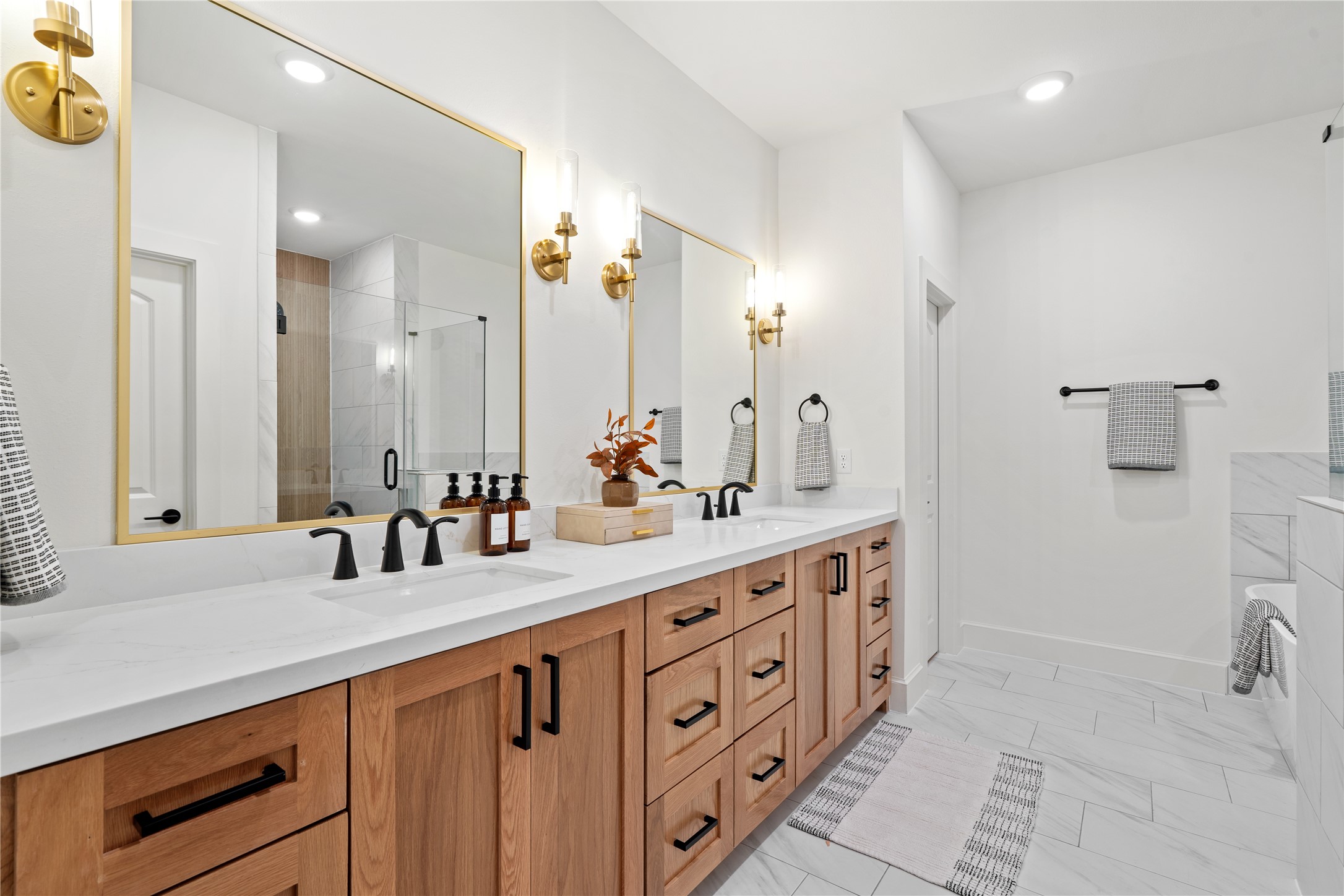 1614 Ojeman Road, Unit J Houston, TX 77055 - Photo 35 of 50 Luxurious primary bathroom featuring a double vanity with quartz countertops, modern matte black fixtures, and elegant gold-accented mirrors - combining warmth and sophistication in one space.