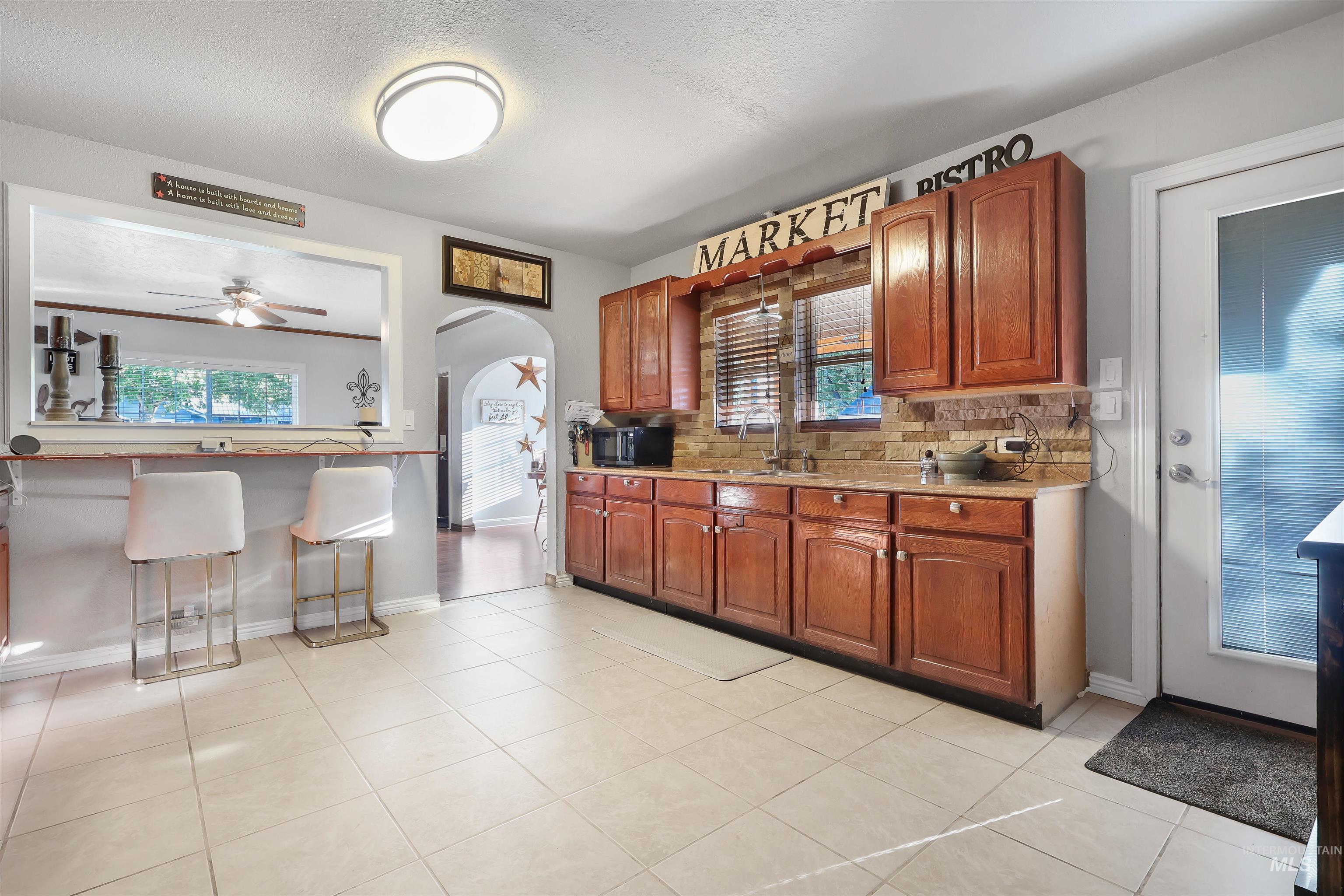 1009 9th Street Rupert, ID 83350 - Photo 8 of 28 Tile flooring, wood cabinets, stone backsplash, pass-through opening, and an arched doorway