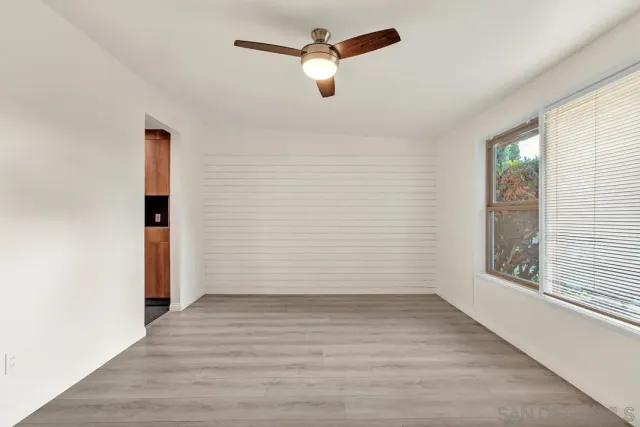 an empty room with wooden floor chandelier fan and windows