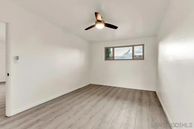 an empty room with wooden floor ceiling fan and windows