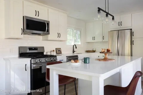 a kitchen with stainless steel appliances a stove a sink dishwasher a refrigerator white cabinets and wooden floor
