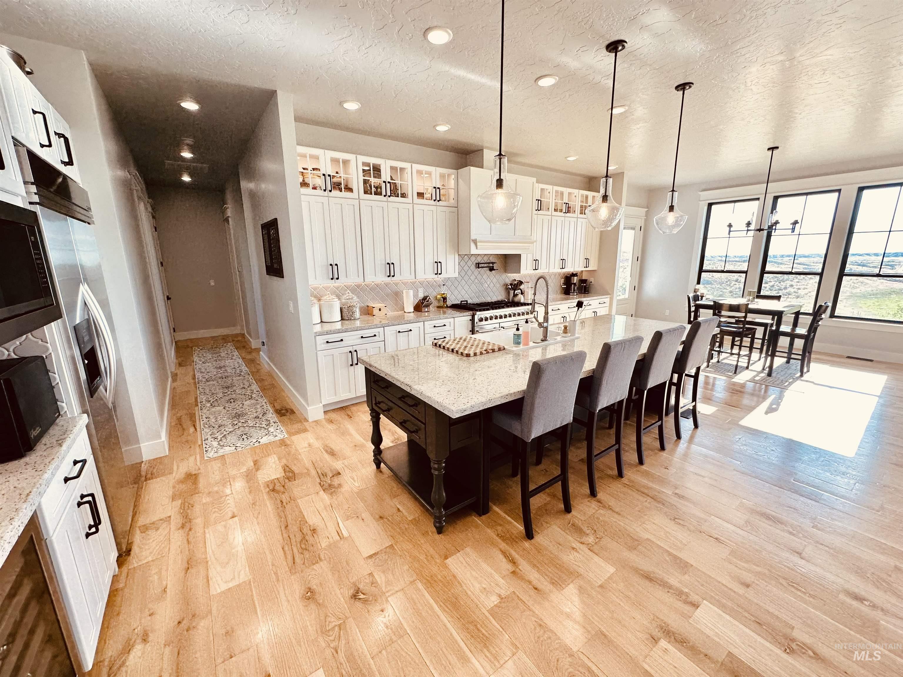 876 Coyote Gulch Road Adrian, OR 97901 - Photo 11 of 50 Gourmet kitchen featuring a large island with seating, pendant lighting, built-in appliances, white cabinetry, and wood-finish flooring