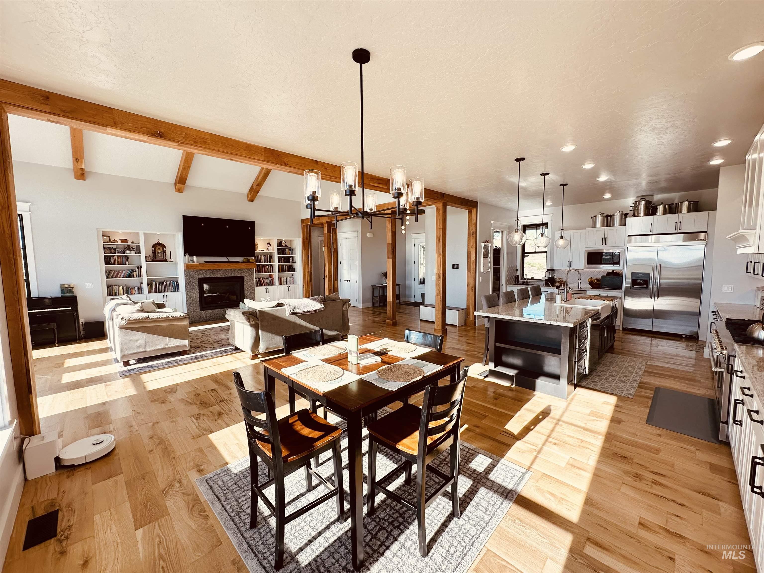 876 Coyote Gulch Road Adrian, OR 97901 - Photo 17 of 50 Open-concept living area with wood-finish flooring, exposed ceiling beams, and a stone-surround fireplace flanked by built-in shelving