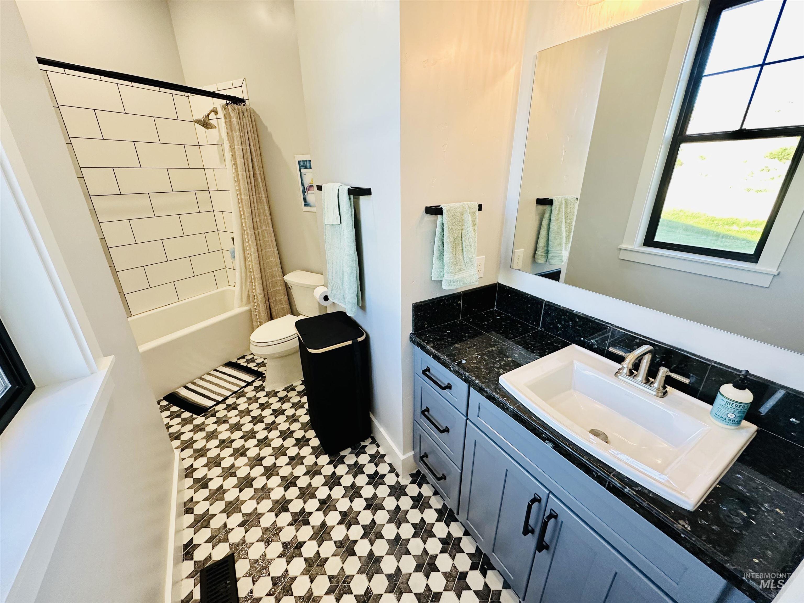 876 Coyote Gulch Road Adrian, OR 97901 - Photo 25 of 50 Bathroom featuring a patterned hexagonal floor tile, a dark granite-look countertop, gray vanity cabinetry with black hardware, a rectangular undermount sink, and a shower-tub combination with subway tile surround