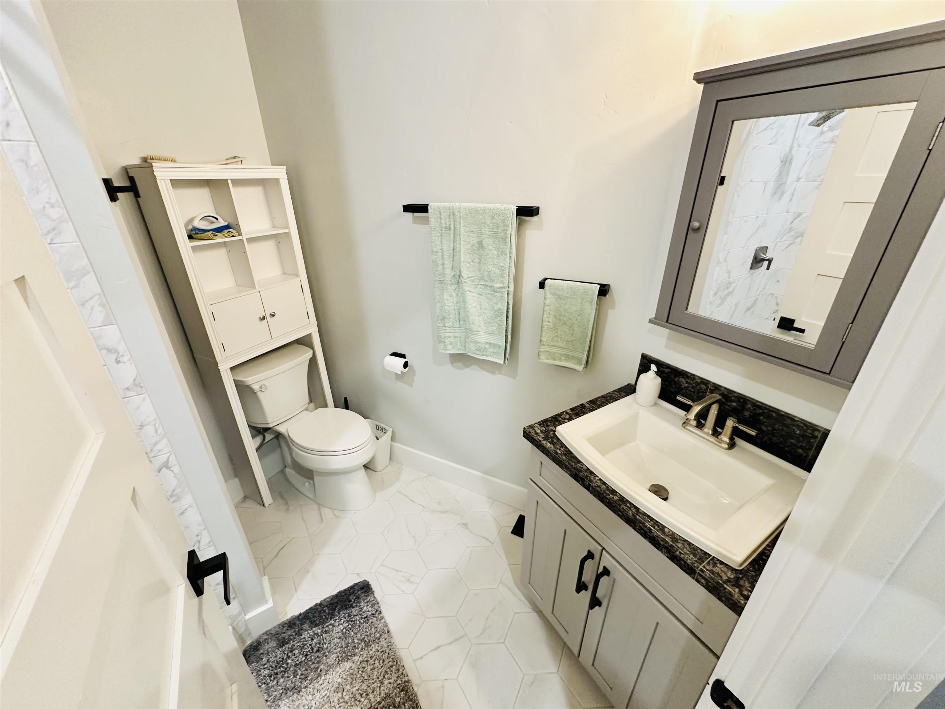 876 Coyote Gulch Road Adrian, OR 97901 - Photo 34 of 50 Bathroom featuring a white hexagonal tile floor, dark granite-finish countertop, and a gray vanity with black hardware