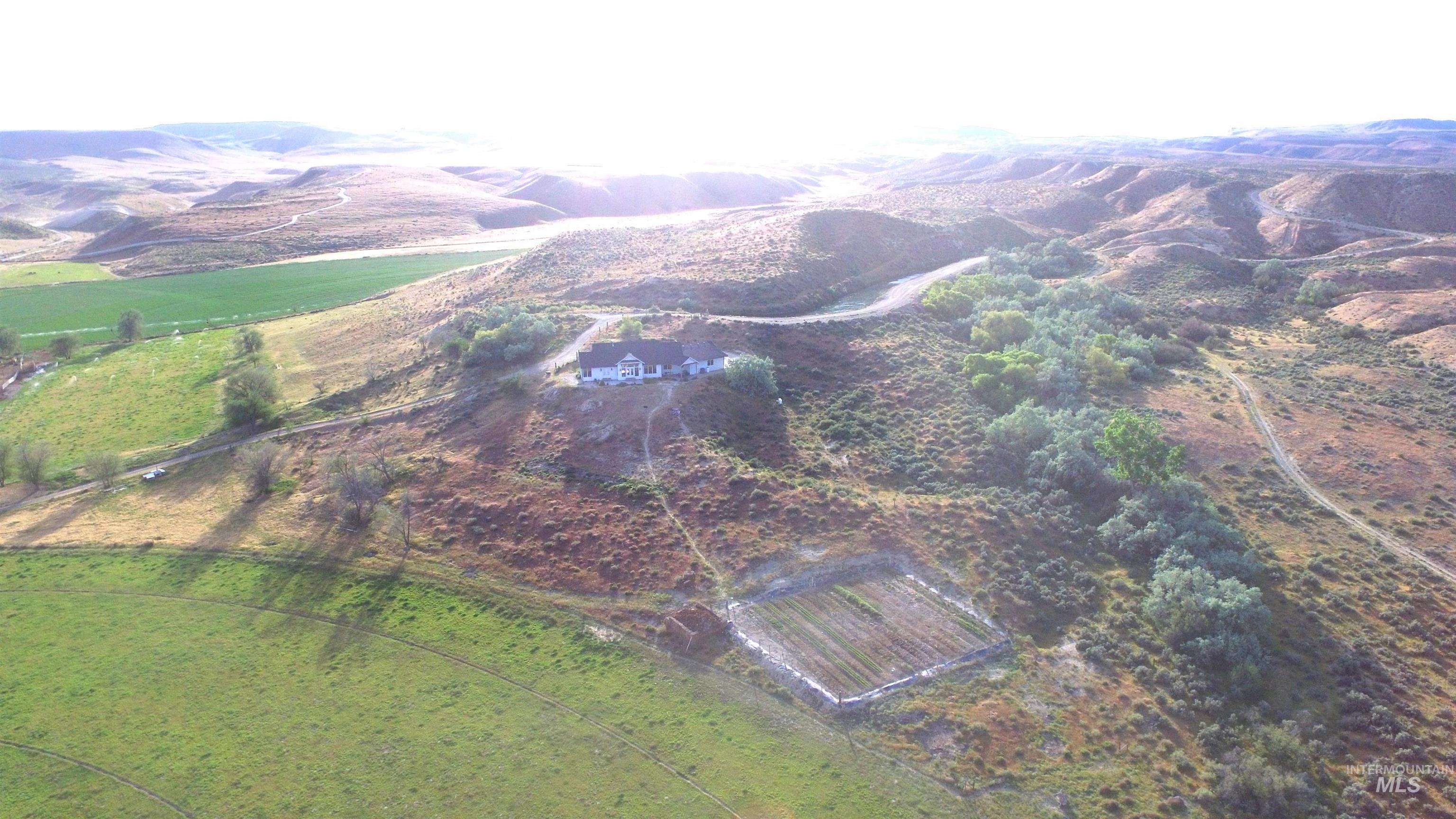 876 Coyote Gulch Road Adrian, OR 97901 - Photo 50 of 50 Expansive rural landscape featuring a white-sided home with a dark roof, surrounded by varied terrain including green fields, scrubland, and a treelined watercourse