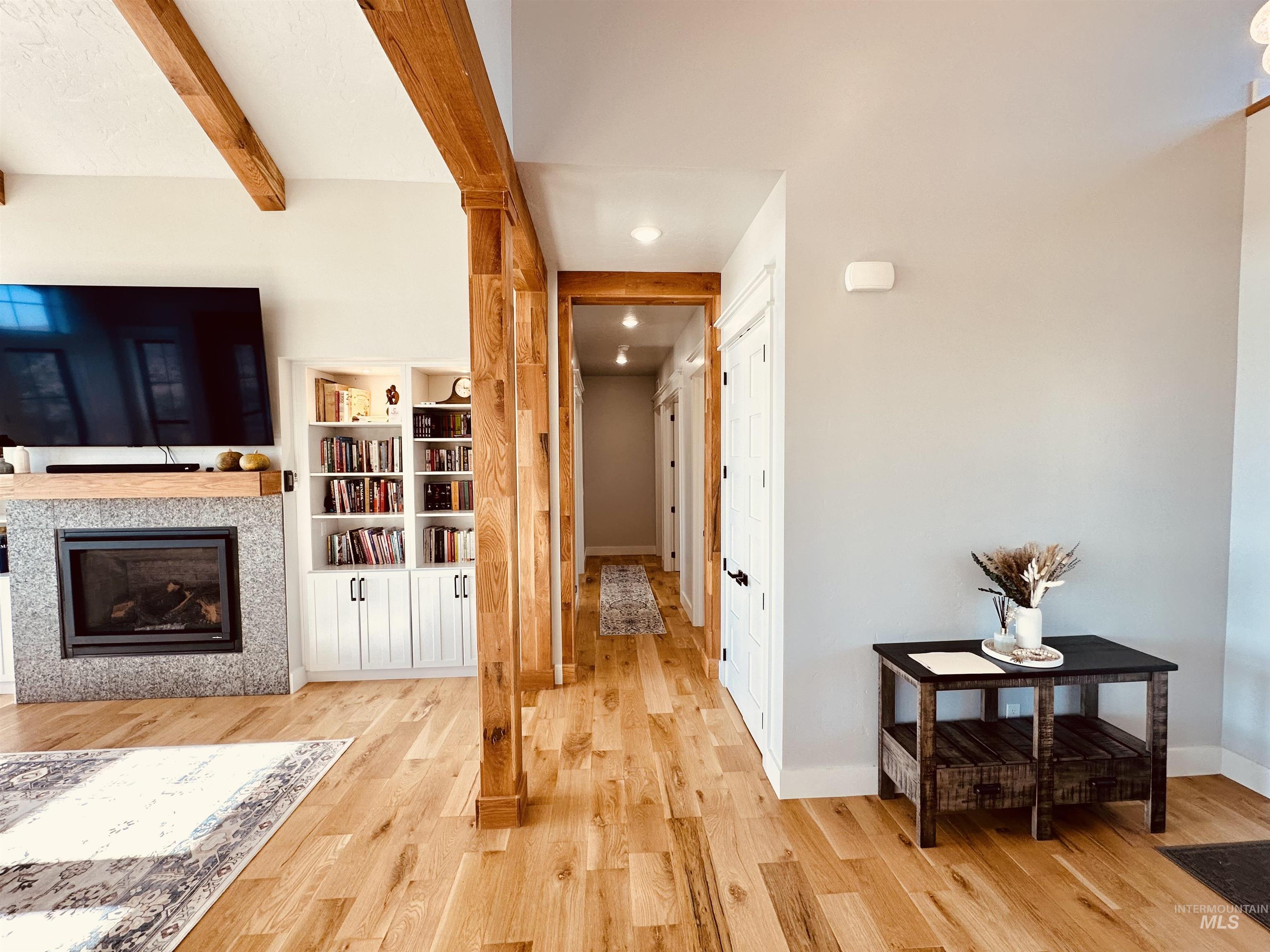 876 Coyote Gulch Road Adrian, OR 97901 - Photo 10 of 50 Open-concept living area featuring exposed wood beams, a fireplace with a stone surround, built-in white cabinetry, and light wood-finish flooring throughout