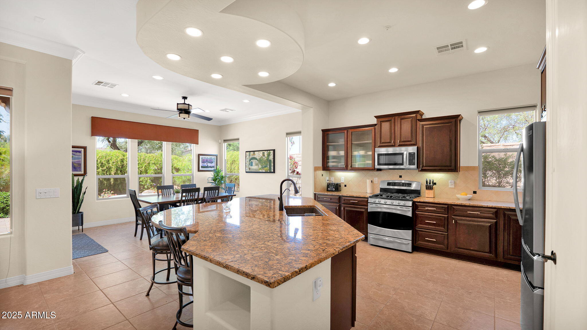 12981 West Yellow Bird Lane Peoria, AZ 85383 - Photo 24 of 47 a kitchen with kitchen island granite countertop a stove a sink a dining table and chairs with wooden floor