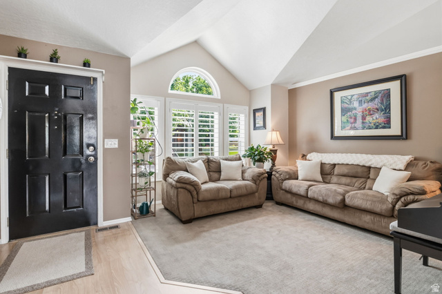 1101 Old Dairy Road Sandy, UT 84094 - Photo 7 of 36 Vaulted ceiling living area featuring a large arched window, multiple windows with 4 in. plantation shutters, light wood-finish flooring, and a black paneled entry door