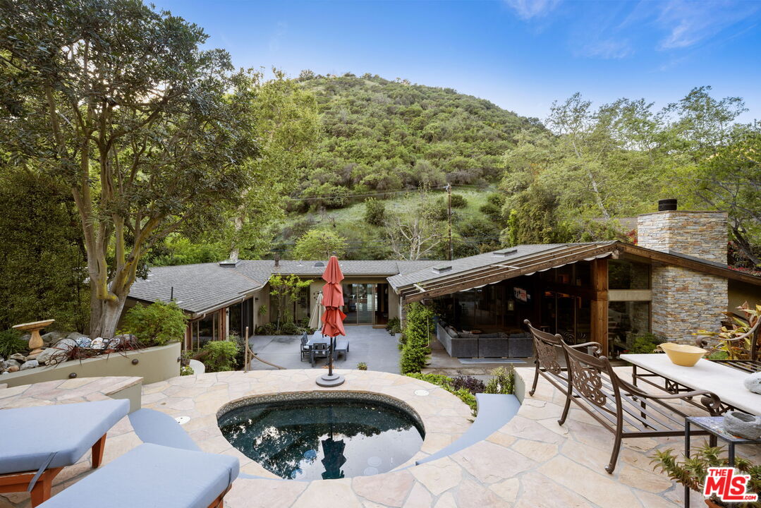 2618 Mandeville Canyon Road Los Angeles, CA 90049 - Photo 32 of 45 a view of a patio with couches table and chairs under an umbrella with a small yard