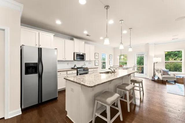 a kitchen with stainless steel appliances granite countertop a refrigerator a sink a stove a dining table and chairs with wooden floor