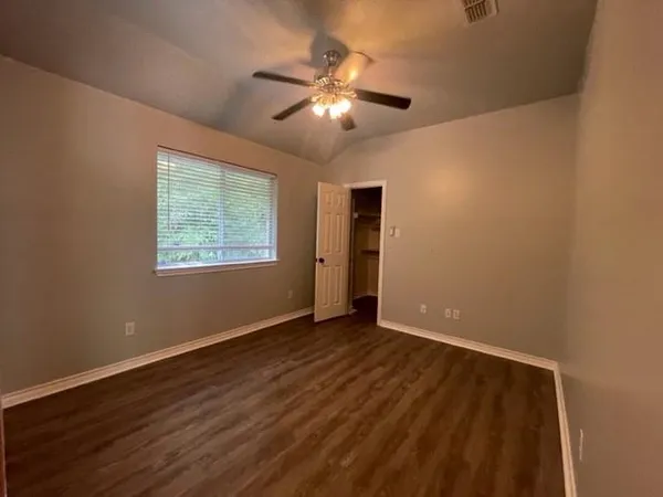 a view of an empty room with wooden floor and a chandelier fan