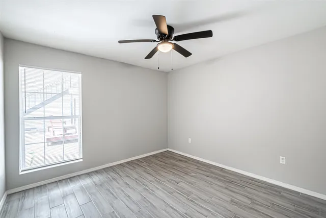 an empty room with wooden floor ceiling fan and windows