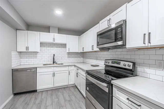 a kitchen with stainless steel appliances a sink dishwasher a stove top oven a refrigerator with white cabinets and wooden floor