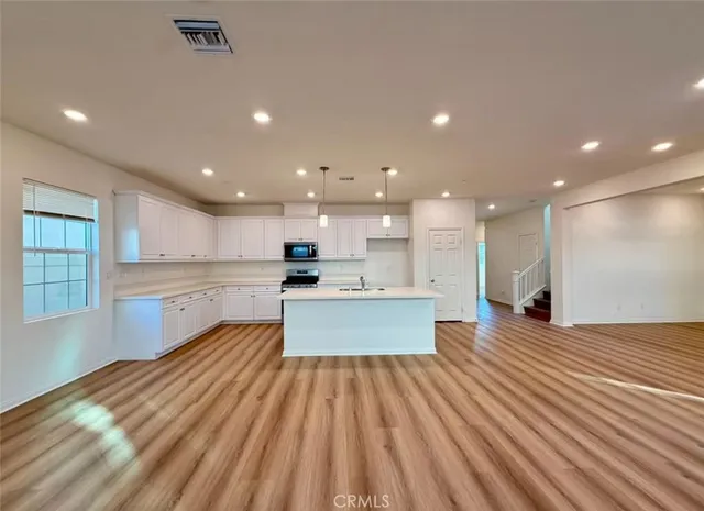 a large kitchen with kitchen island a stove a sink dishwasher and white cabinets with wooden floor