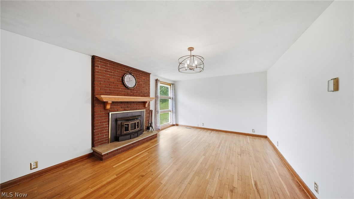 89 Dagg Road Parkersburg, WV 26101 - Photo 16 of 45 Living area featuring a brick fireplace with a wood-burning insert, a wood mantel, light wood-finish flooring, and a contemporary chandelier