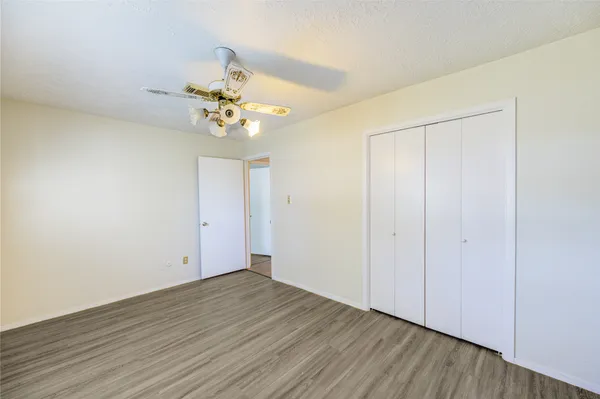 a view of an empty room with chandelier fan and wooden floor