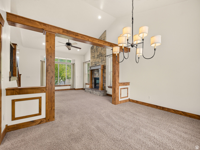 1279 West 1500th Street North Mapleton, UT 84664 - Photo 16 of 83 Vaulted ceiling with an eight-light chandelier, a stone-surround fireplace, wood-finish beams, white wall paneling, and large windows