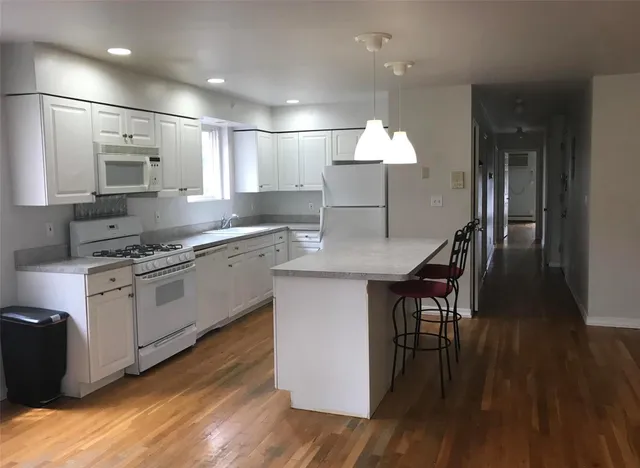 a kitchen with kitchen island granite countertop wooden floors and white cabinets