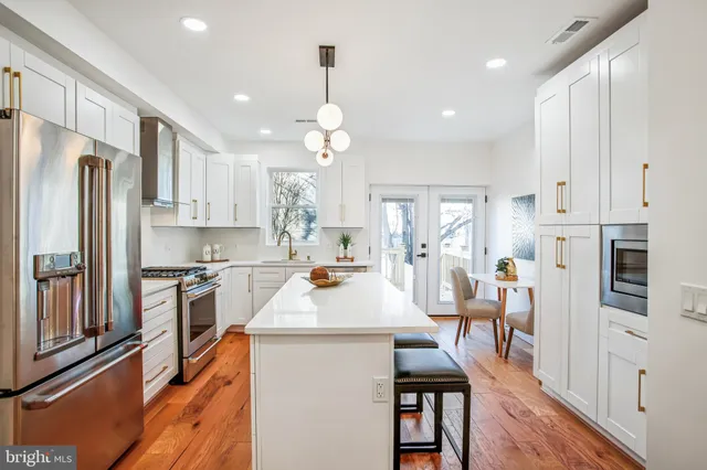 a large kitchen with stainless steel appliances kitchen island granite countertop a refrigerator a stove a sink a dining table and chairs with wooden floor
