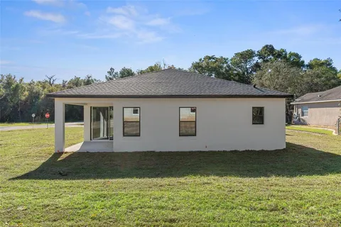 a house that is sitting in the grass with large trees and sky view