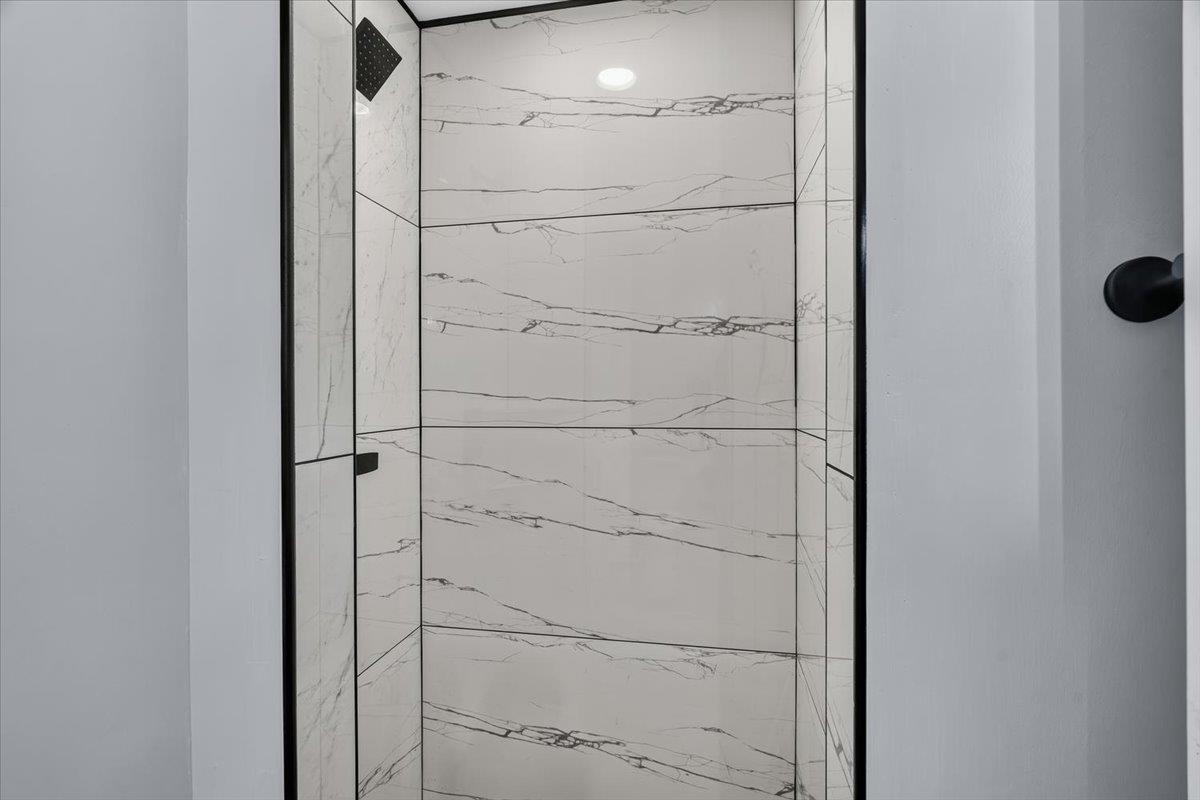 1744 West Holmes Road Memphis, TN 38109 - Photo 13 of 24 Modern walk-in shower featuring large-format porcelain tile walls with linear veining, frameless glass enclosure with matte black hardware, and integrated ceiling-mounted showerhead