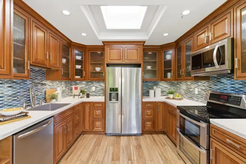 a kitchen with stainless steel appliances granite countertop a refrigerator a sink dishwasher a stove and a dining table with wooden floor