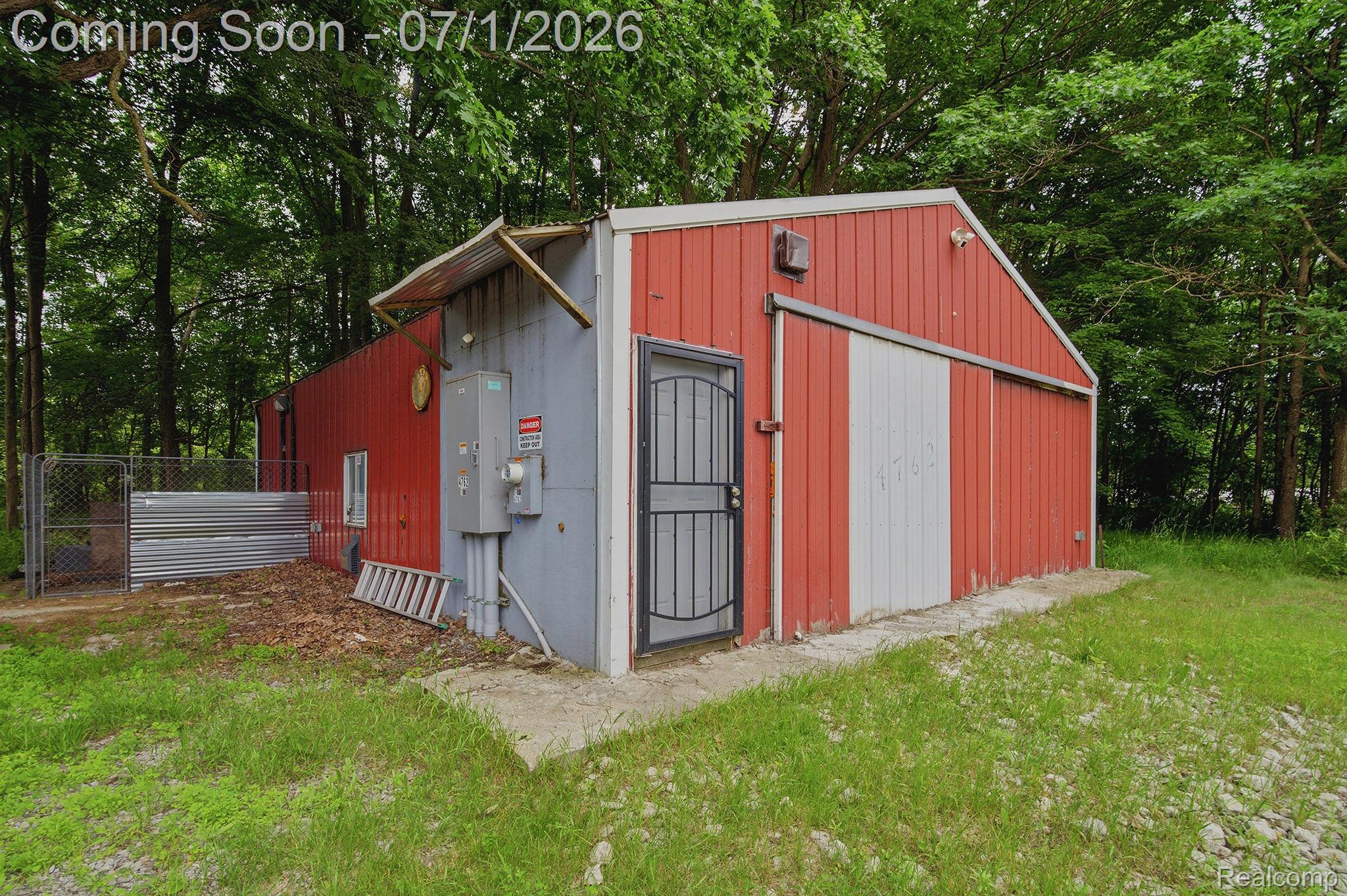 4762 Lonsberry Road Columbiaville, MI 48421 - Photo 32 of 36 Red and gray metal-sided auxiliary building featuring a sliding white door, an exterior door with a security screen, and a chain-link fenced area