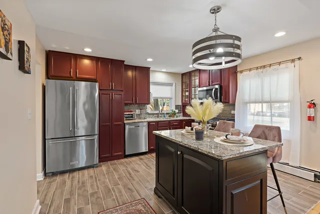 a kitchen with stainless steel appliances granite countertop a refrigerator a sink dishwasher a stove and a dining table with wooden floor