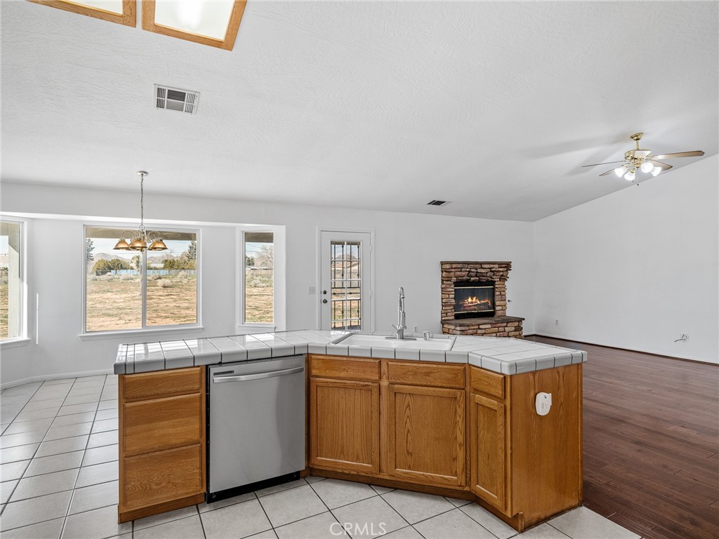 14266 Kiowa Road Apple Valley, CA 92307 - Photo 14 of 27 Open kitchen and dining area with abundant natural light and views of the expansive backyard. Features tile flooring, ample cabinetry, and a new stainless steel dishwasher and microwave.