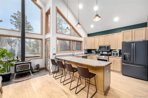 a kitchen with stainless steel appliances granite countertop a stove a refrigerator a sink a dining table and chairs with wooden floor