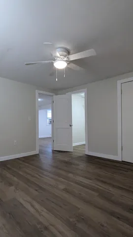 a view of an empty room with wooden floor and a ceiling fan