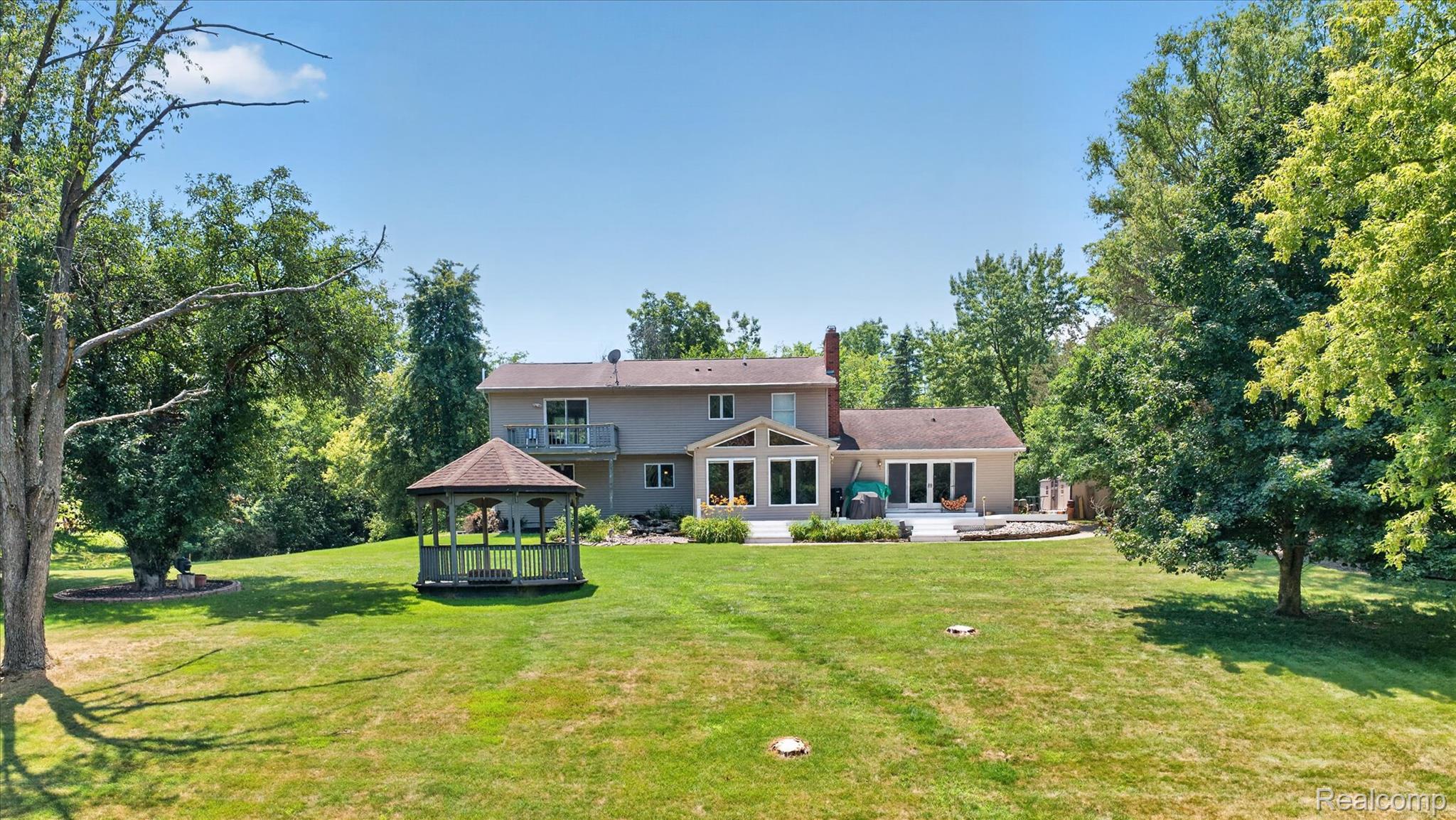 7186 East River Road Flushing, MI 48433 - Photo 28 of 47 Expansive backyard featuring a large green lawn, mature trees, and a freestanding gazebo with a shingled roof