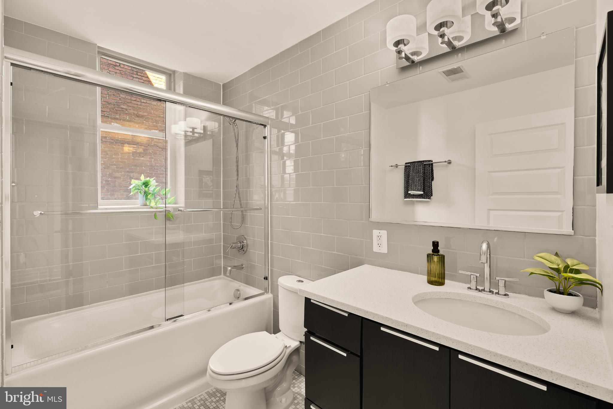 1811 Wyoming Avenue Northwest, Unit 32 Washington, DC 20009 - Photo 19 of 26 a bathroom with a granite countertop sink a toilet a mirror a bathtub and shower