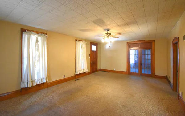 an empty room with chandelier fan and windows