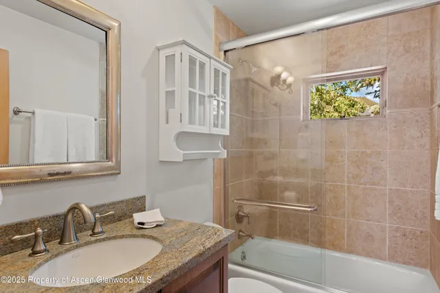a bathroom with a granite countertop sink a mirror a bathtub and shower