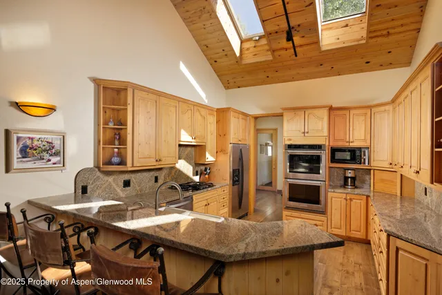 a room with stainless steel appliances kitchen island granite countertop a table chairs and a refrigerator
