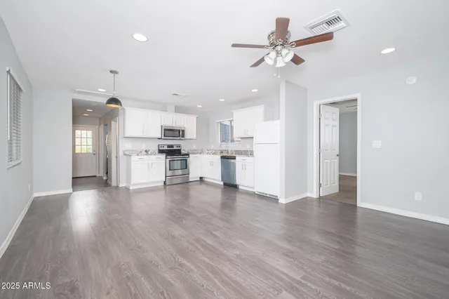 a view of an empty room with kitchen appliances and a ceiling fan