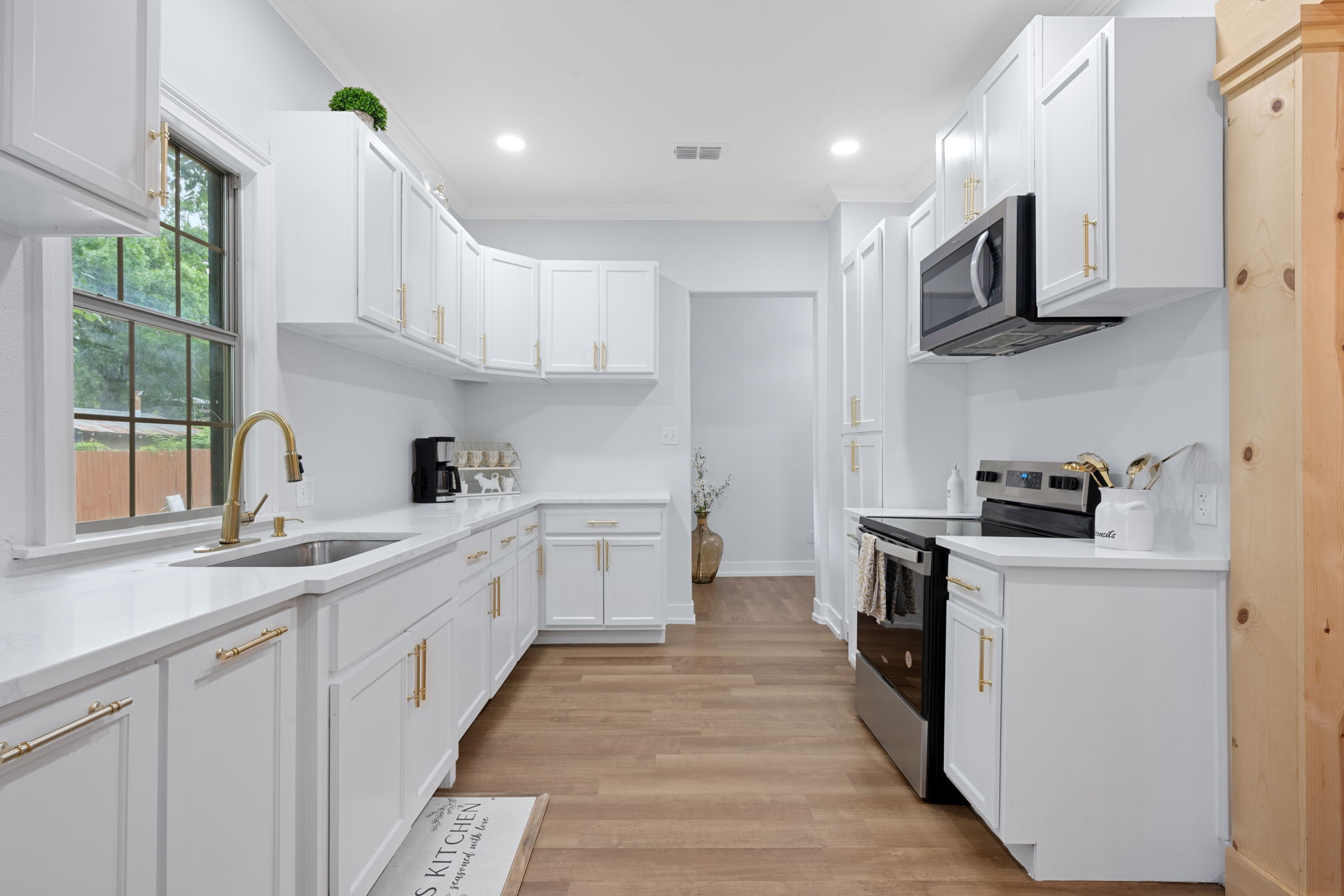 602 East 6th Street Cameron, TX 76520 - Photo 18 of 40 White kitchen cabinetry with gold-tone hardware, wood-finish flooring, stainless steel appliances, and a window over the sink