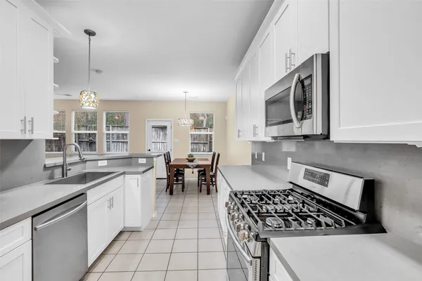 a kitchen with stainless steel appliances granite countertop a stove top oven a sink a dining table and chairs with white cabinets