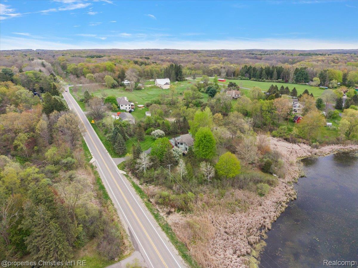 6175 Tripp Road Holly, MI 48442 - Photo 50 of 63 Waterfront property featuring a wooded landscape, direct water frontage, a paved road, and a distant barn structure