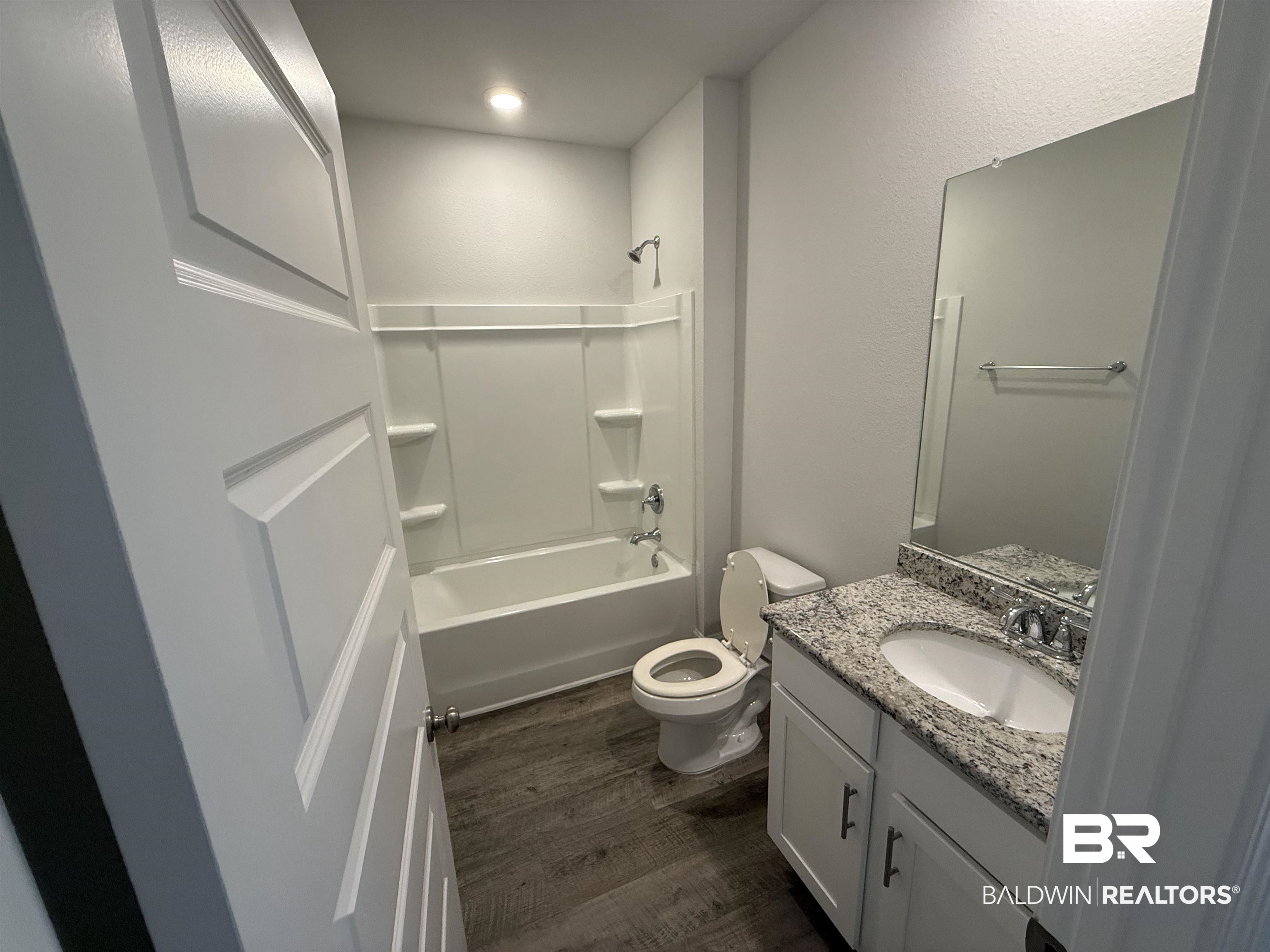 23247 Lieutenant Avenue Foley, AL 36535 - Photo 10 of 47 Bathroom featuring a white bathtub with integrated shelving, a dual-flush toilet, and wood-finish flooring
