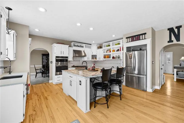 a kitchen with stainless steel appliances kitchen island granite countertop a refrigerator a stove a sink dishwasher and white cabinets with wooden floor