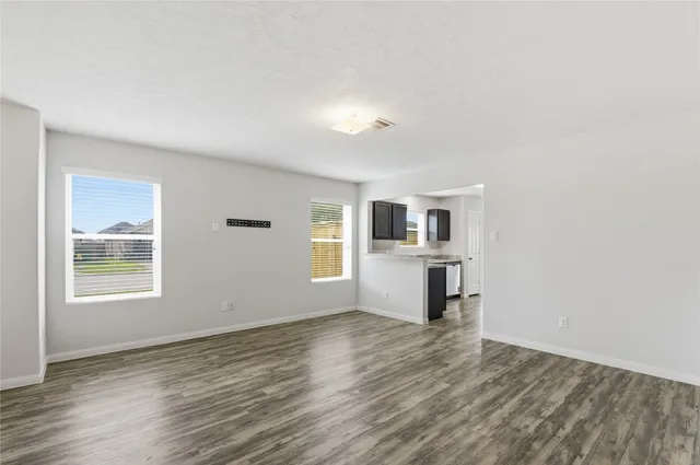 a view of a kitchen and an empty room with wooden floor and a window