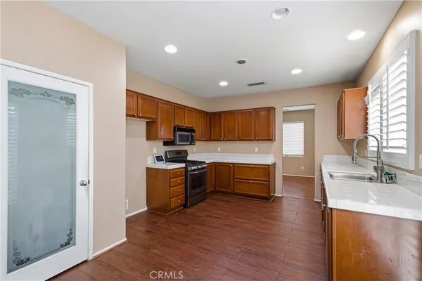 a kitchen with stainless steel appliances granite countertop wooden cabinets a sink dishwasher a stove and a refrigerator with wooden floor