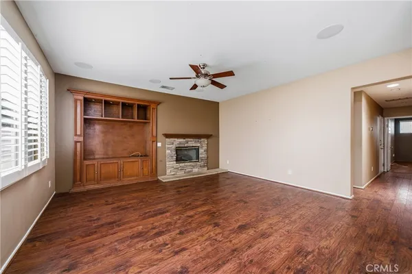 an empty room with wooden floor a ceiling fan and windows