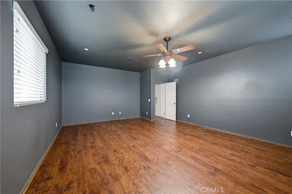 a view of an empty room with wooden floor and a ceiling fan